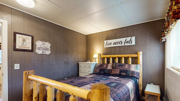 A bedroom with a wooden bed frame, a quilted bedspread, a small dresser, and a wall sign that reads "love never fails". - Moose Hollow Apartment (Greenville)