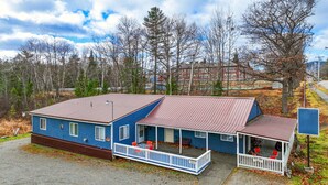 A two-story building with a blue exterior and a red roof, featuring a porch with red chairs and a small table. - Moose Hollow Apartment (Greenville)