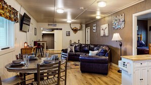A cozy living room with a dark leather couch, a dining table set with plates and glasses, and a kitchen area in the background. - Moose Hollow Apartment (Greenville)