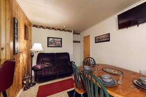 A cozy dining area with a wooden table set for four, a dark red sofa, and a red rug.