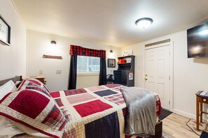 A bedroom with a bed, a desk, a chair, a television, and a door.