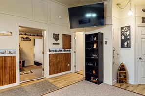 Una habitación con suelo de madera, una estantería negra, un televisor montado y una puerta decorada con una cabeza de oso.