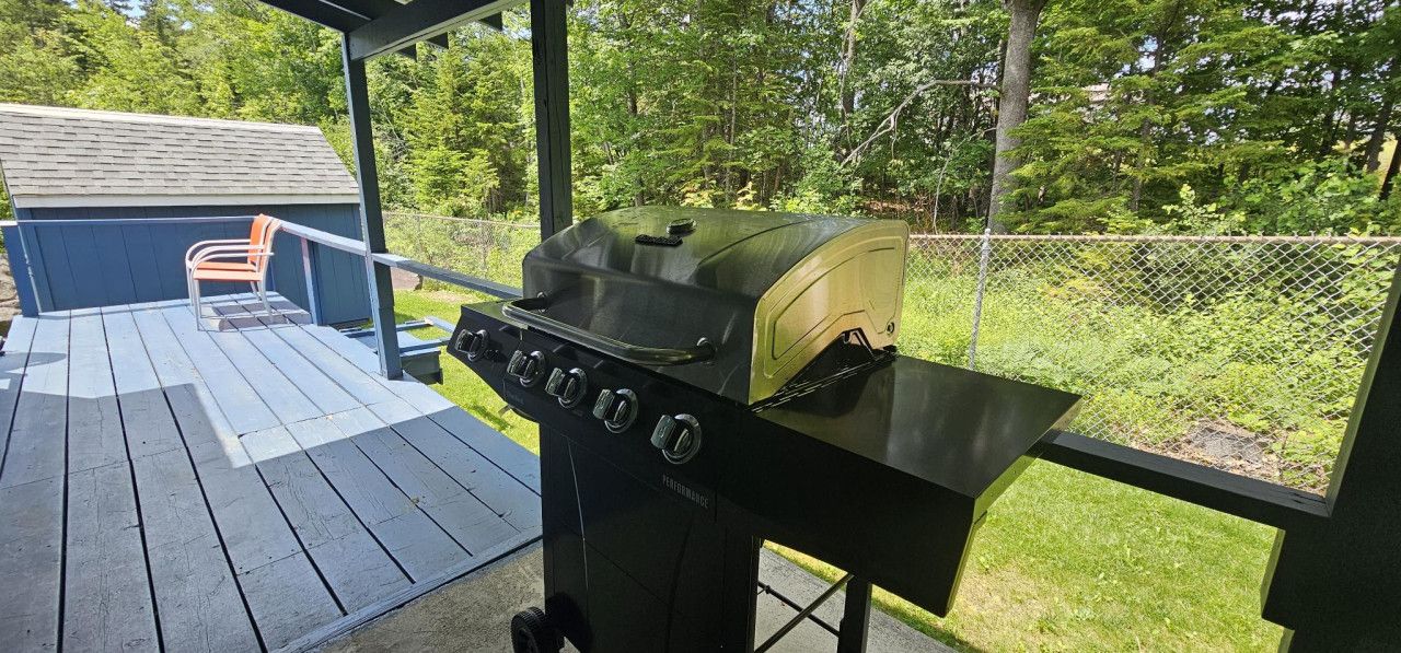 En grill på en træterrasse med en stol og en bygning i baggrunden.