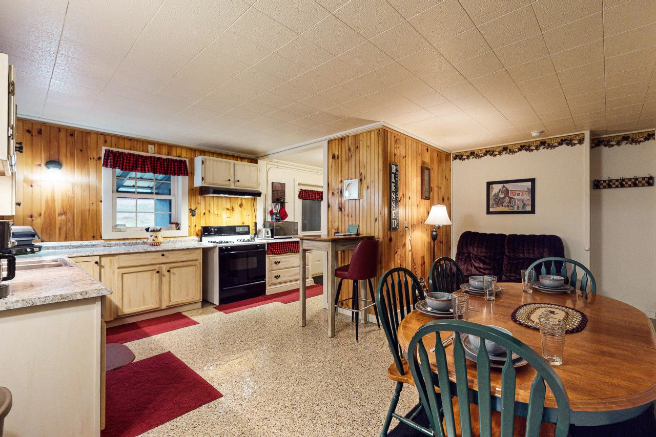 A compact kitchen with wooden cabinets, a dining table with chairs, and a red rug.