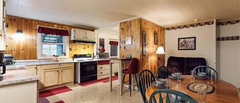 A compact kitchen with wooden cabinets, a dining table with chairs, and a red rug.