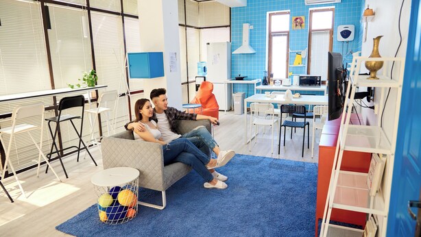 A modern living room with a sofa, a dining table, and a kitchen area in the background. - Caravan  (Turkestan)