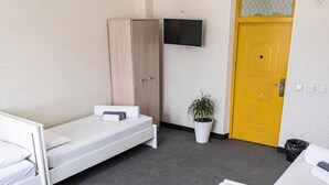 A hotel room with a bed, a wardrobe, a television mounted on the wall, and a yellow door. - Caravan  (Turkestan)