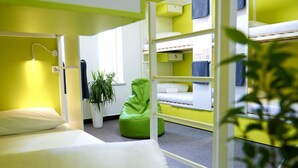 A dormitory room with bunk beds, a green bean bag chair, a potted plant, and a white desk. - Caravan  (Turkestan)