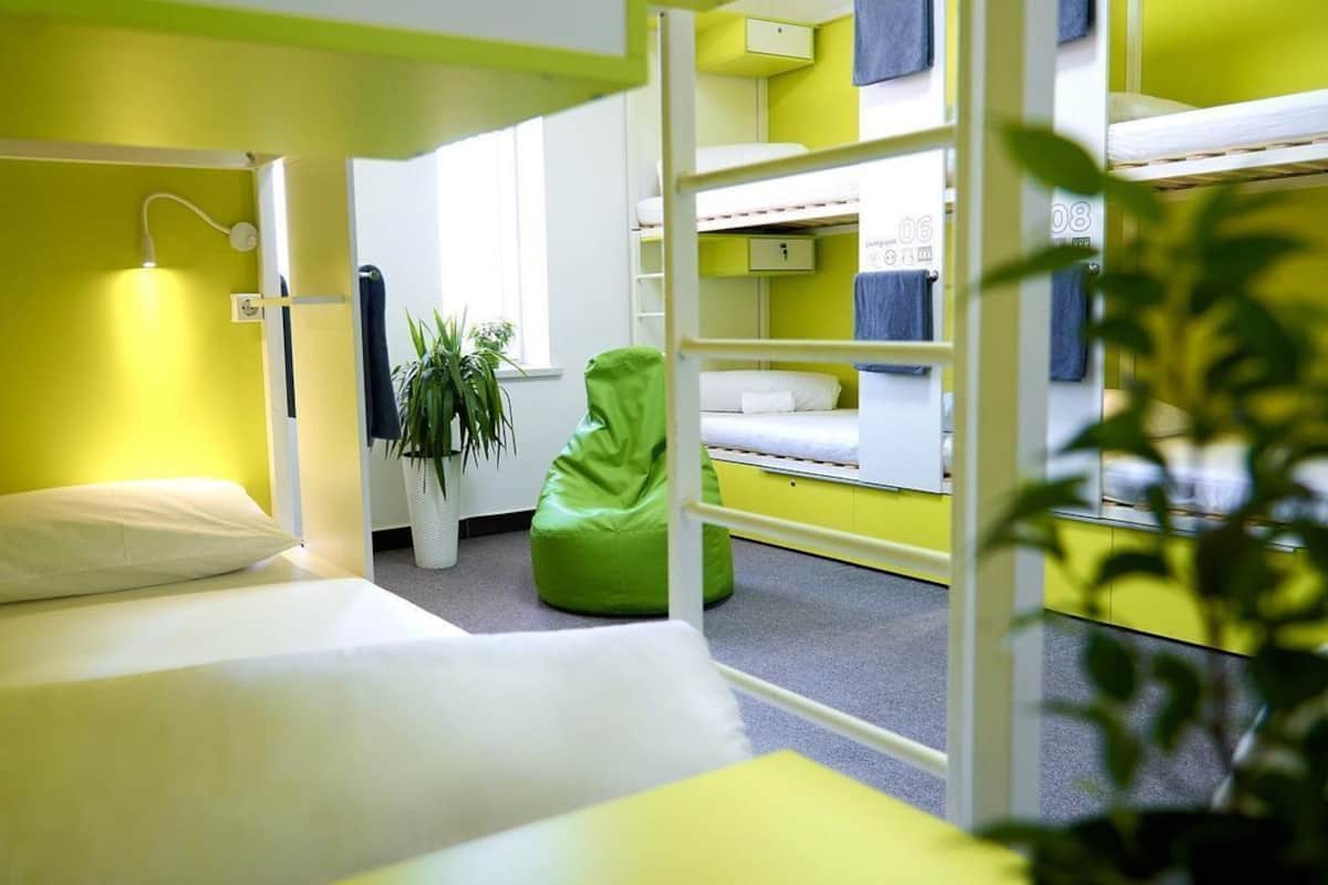 A dormitory room with bunk beds, a green bean bag chair, a potted plant, and a white desk.