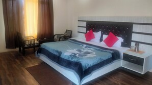 A bedroom with a bed, a nightstand, a chair, and a window with curtains. - The Shagun Grand (Rohtak)