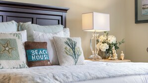 A neatly made bed with multiple pillows, a bedside lamp, and a small table with flowers and figurines. - 30A Condo + Gulf Views, Pools, Grill & Bikes (Santa Rosa Beach)