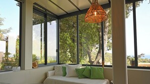 A room with a large window, a white sofa with green cushions, and a woven pendant light.