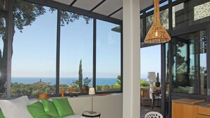 A bedroom with a large window offering a view of the sea and greenery.