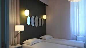 A hotel room with two beds, a bedside table with a lamp, and a wall with oval-shaped light fixtures.