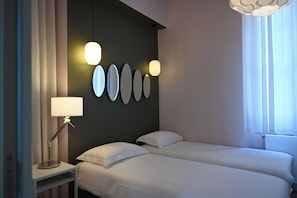 A hotel room with two beds, a bedside table with a lamp, and a wall with oval-shaped light fixtures. - VILLA ALFONSA - APARTMENT "L'ATELIER" sea view, Garden level South-East (Saint-Raphaël)