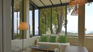 A modern living room with a sofa, two chairs, a small table, and large windows offering a view of trees and hills.