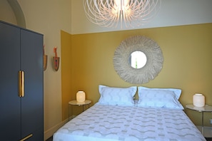 A bedroom with a bed, a wardrobe, a round mirror, and two bedside tables with lamps.