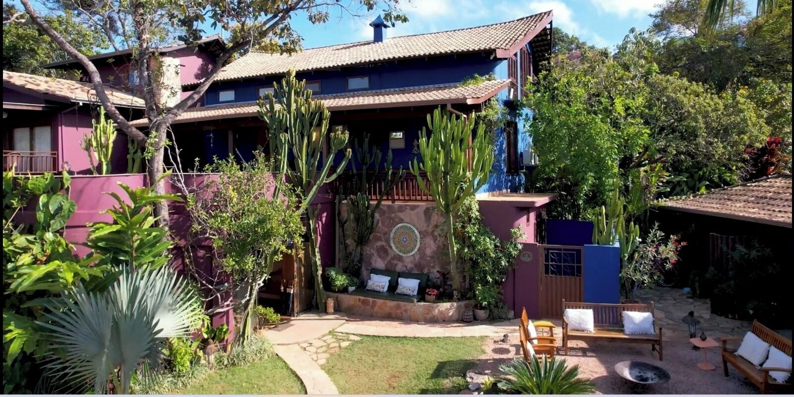 A two-story house with a patio area, surrounded by various plants and cacti.