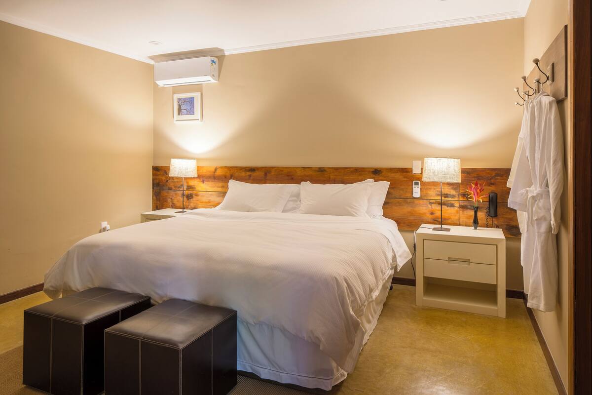 Habitació d'hotel amb un llit gran, dues taules de nit, una banca i un panell de fusta al capçal.