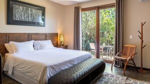 A bedroom with a bed, a wooden headboard, a nightstand with a lamp, a chair, and a view of the outdoors through a sliding glass door. - Pousada Maya (Alto Paraíso de Goiás)