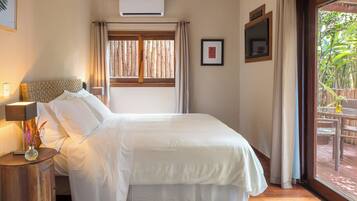 A hotel room with a bed, a nightstand, a lamp, a framed picture, an air conditioner, and a window with curtains.