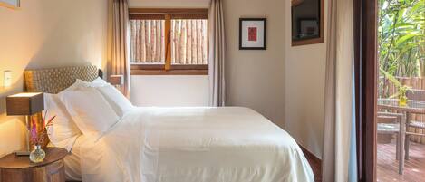 A hotel room with a bed, a nightstand, a lamp, a framed picture, an air conditioner, and a window with curtains.