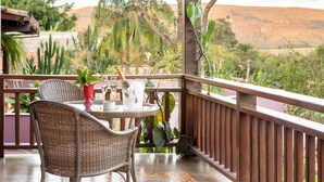A balcony with wicker furniture, a table with a glass, and a view of a desert landscape. - Pousada Maya (Alto Paraíso de Goiás)