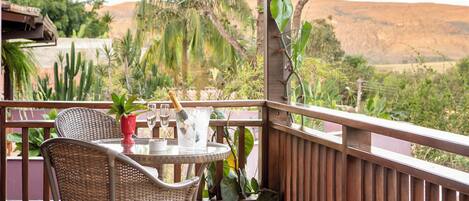 A balcony with wicker furniture, a table with a glass, and a view of a desert landscape.