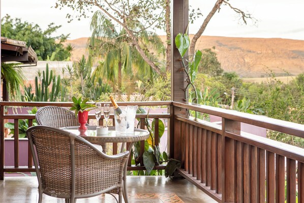 Un balcón con mobiliario de mimbre, una mesa con un vaso y vistas a un paisaje desértico.