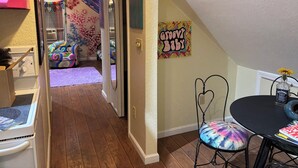 Una habitación acogedora con suelo de madera, una cama colorida, un cuadro y una mesita con una silla.