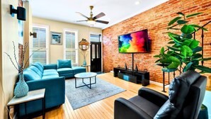 Un salon avec un mur en briques, un ventilateur de plafond, un téléviseur, un canapé, une table basse et une plante.