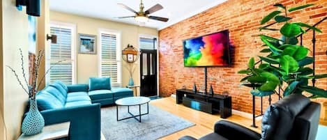 A living room with a brick wall, a ceiling fan, a TV, a sofa, a coffee table, and a plant.