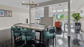 Un espace de salle à manger moderne, avec une longue table et des chaises assorties, un luminaire suspendu au plafond et des œuvres d’art encadrées accrochées au mur.