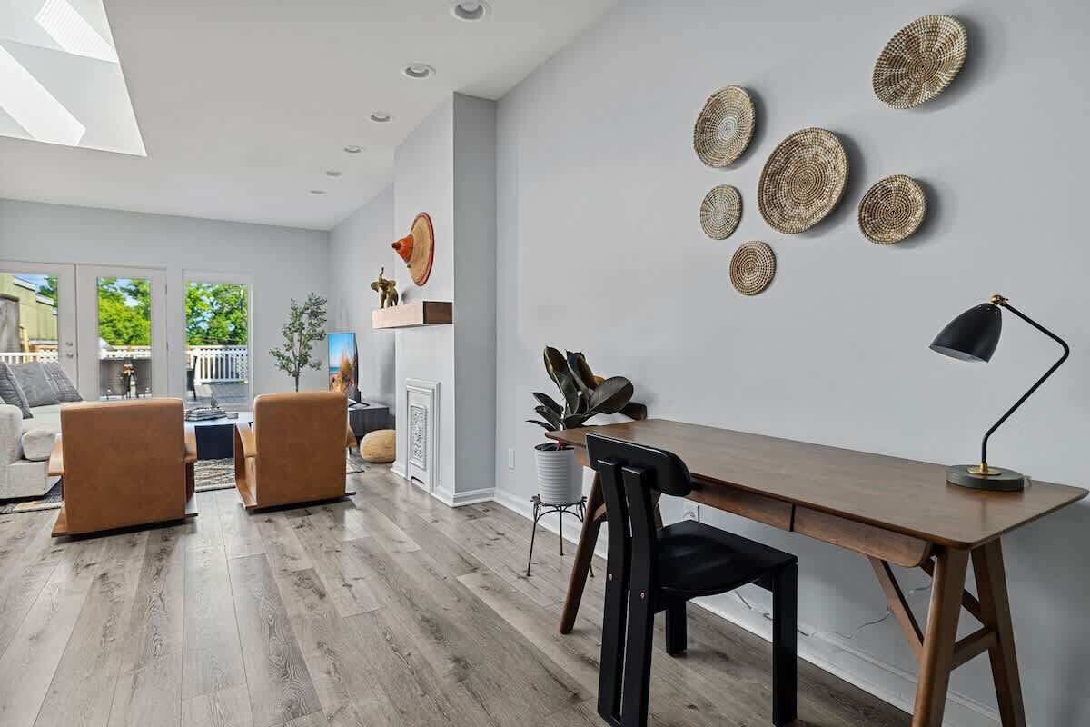 A modern living room with a wooden dining table, two brown armchairs, a black chair, and a black floor lamp.