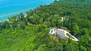 An aerial view of a property with a swimming pool, surrounded by dense forest and a beach. - Juniper Presents: Contemporary 26-Acre Estate, Private Beach, Pool (Stevensville)