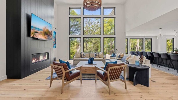 A modern living room with a fireplace, large windows, and a dining area. - Juniper Presents: Contemporary 26-Acre Estate, Private Beach, Pool (Stevensville)