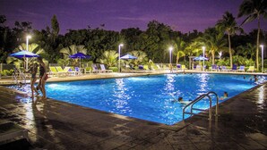 Ein Schwimmbad bei Nacht mit Liegestühlen und Sonnenschirmen.