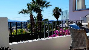 A balcony with a white cushioned lounge chair, a wicker chair, and two wine glasses on a table. - Villa Bibi with Spectacular Sunset and Views (Javea)