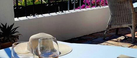 A balcony with a white cushioned lounge chair, a wicker chair, and two wine glasses on a table.