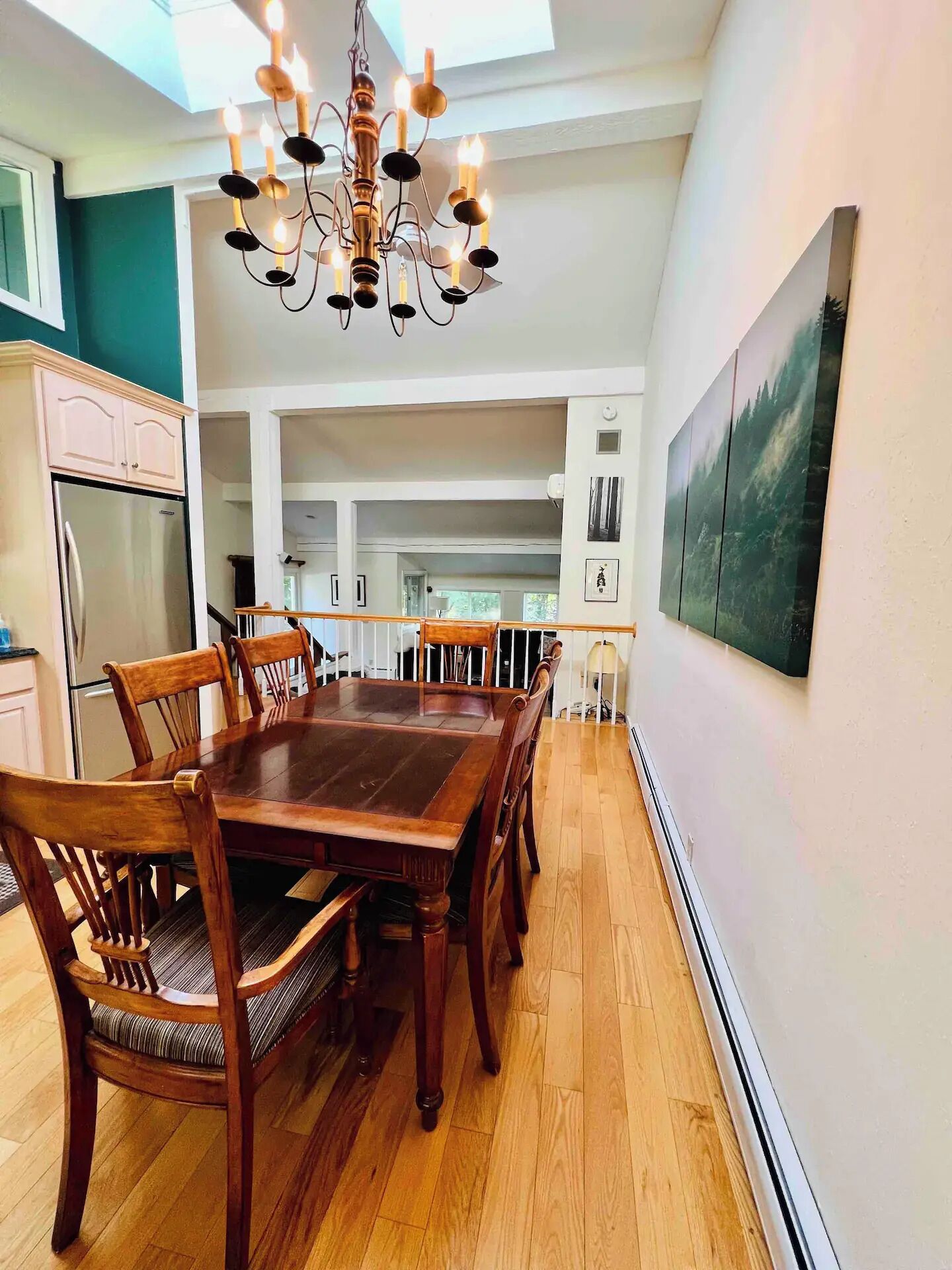 Un coin repas avec une table et des chaises en bois, un lustre et un tableau au mur.
