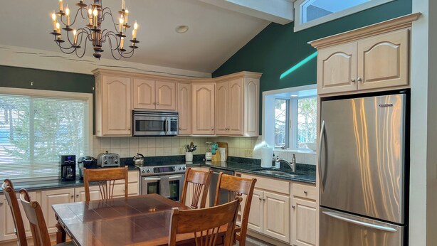 A modern kitchen with white cabinets, stainless steel appliances, a dining table with chairs, and a chandelier.
