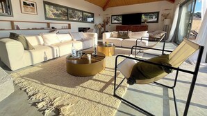 A spacious living room with a high wooden ceiling, a large flat-screen TV, and a comfortable seating area with a sofa and chairs. - Villa San Joseph (Cargès)