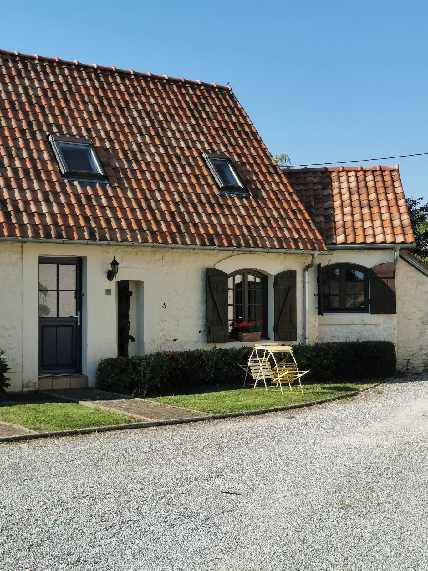 Ein Haus mit Ziegeldach, einer Haustür und einer kleinen Veranda mit Tisch und Stühlen.