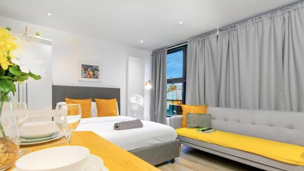 Een moderne hotelkamer met een bed, een bank, een eettafel met borden en glazen, en een raam met gordijnen.