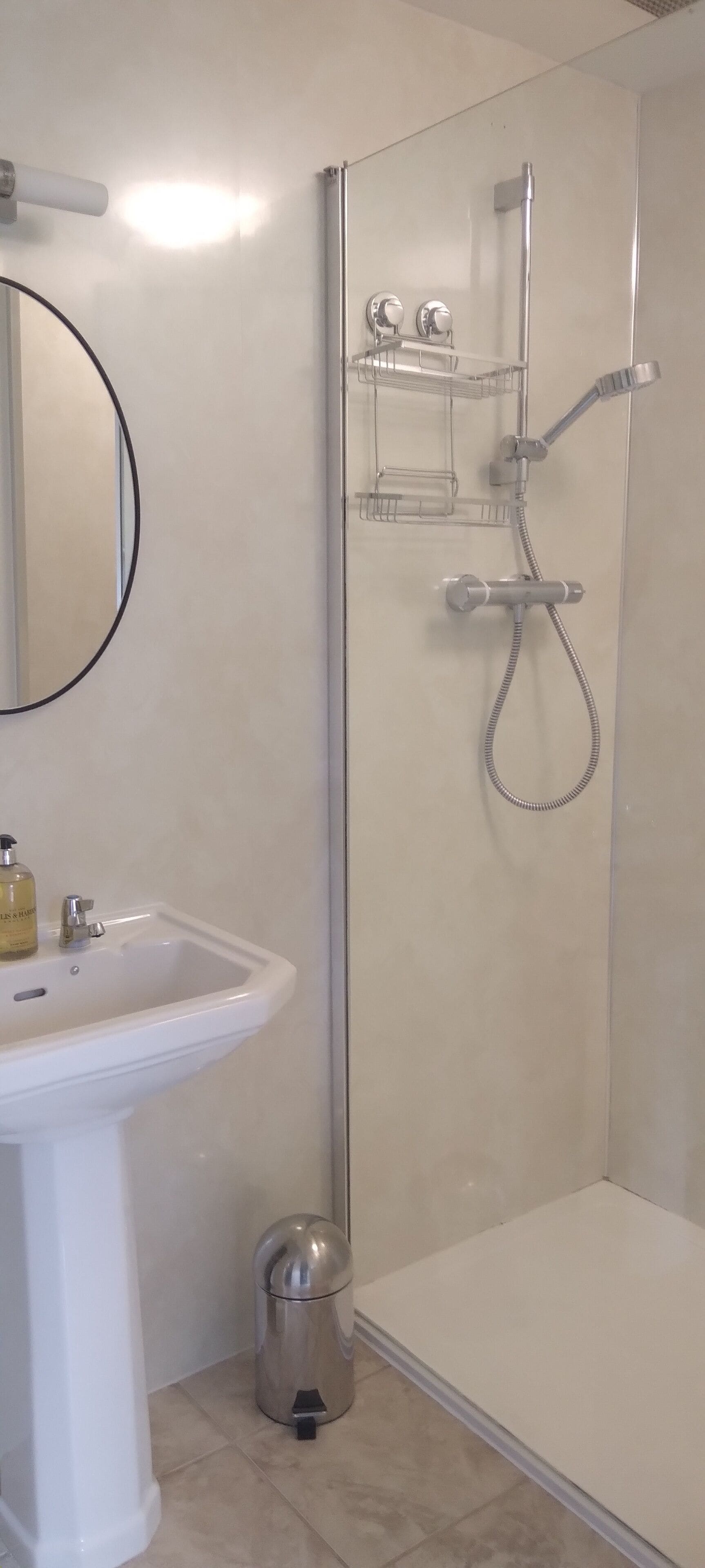 A bathroom with a white sink, a mirror, a shower with a glass door, and a small trash bin.