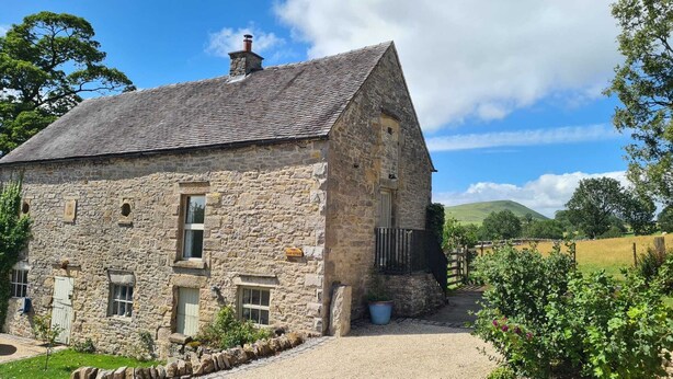 A stone building with a sloped roof, a small porch, and a gravel driveway.