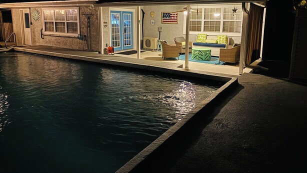 Une maison avec une piscine, une véranda dotée de meubles d’extérieur et un drapeau accroché au mur.