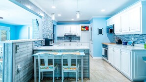 Une cuisine moderne avec des meubles blancs, un pare-feu bleu et un îlot central doté de sièges.
