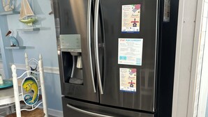 Un réfrigérateur Samsung en acier inoxydable, doté d’un distributeur d’eau, de deux tiroirs et de plusieurs autocollants, dont un pour la série de concerts d’été et un autre avec le slogan « Restez à la page sur les dernières nouveautés en matière de circuits imprimés ».