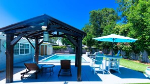 Un'area esterna coperta con piscina, poltrona prendisole e tavolo con ombrellone.